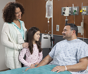 Woman and girl visiting man in hospital bed.