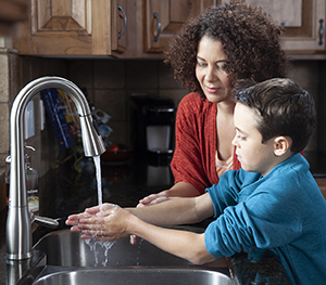 Woman helping boy wash hands in kitchen sink.