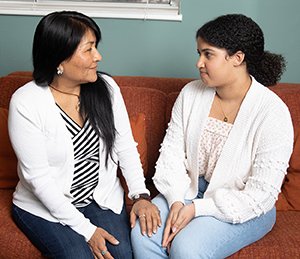 Woman and teen girl sitting on couch talking.