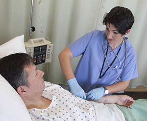 Man in hospital bed, healthcare provider checking his IV.