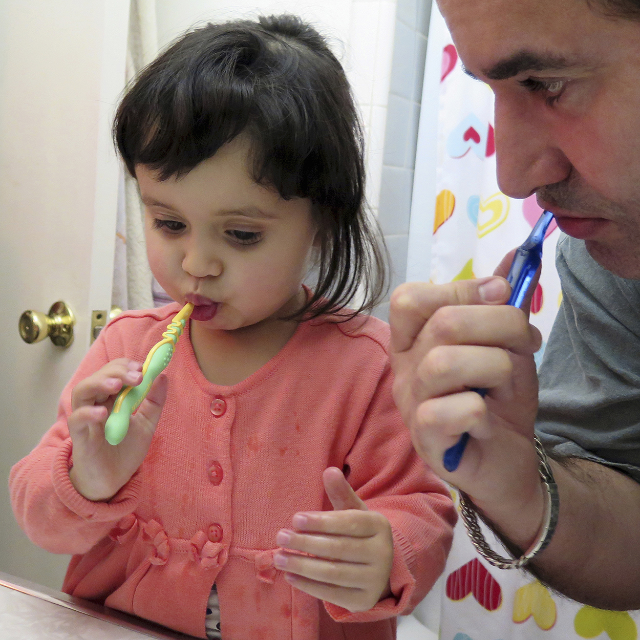 Man and toddler girl brushing teeth in bathroom.