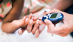 Closeup of adult hands holding glucometer next to child's finger.