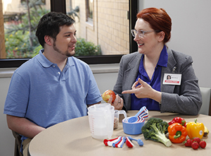 Healthcare provider talking to man. Measuring cups and spoons, fruits and vegetables are on table.