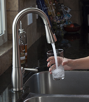 Closeup of hand filling glass with water at kitchen sink.